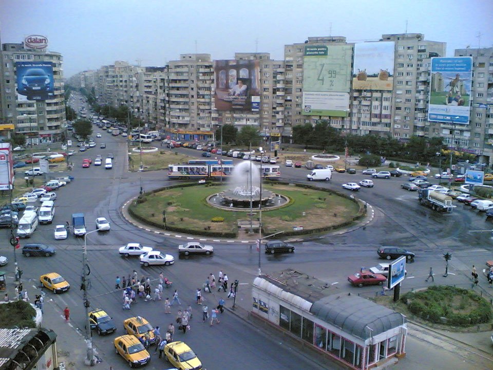 Busy roundabout in Bucharest with fountain and apartment blocks, showcasing urban life in Romania