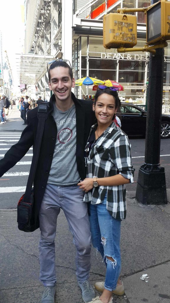 Young people smiling on a New York City street corner near Dean & DeLuca, with a colorful umbrella vendor in the background