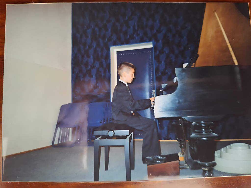 Young boy in a suit playing grand piano on stage during a music recital
