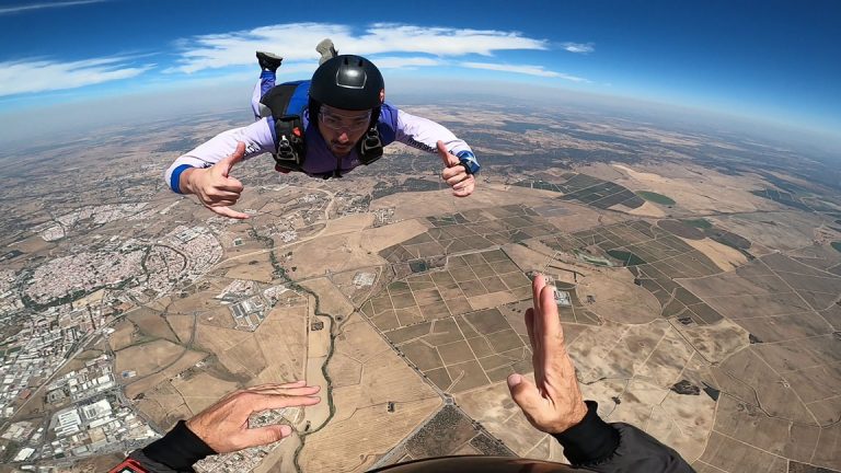 A skydiver's first-person view during freefall shows the ground far below, feeling the exhilarating surprise that skydiving is not as scary as they thought.
